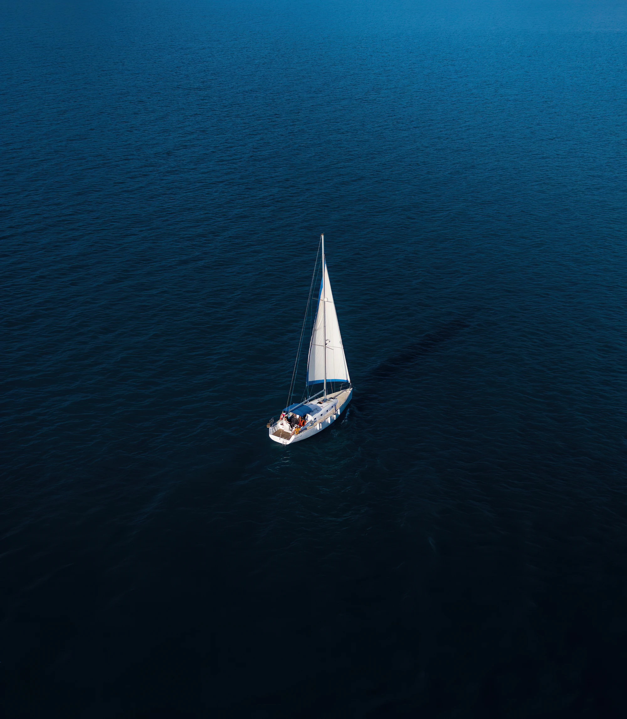 Een zeilboot met witte zeilen op open, diepblauw water
